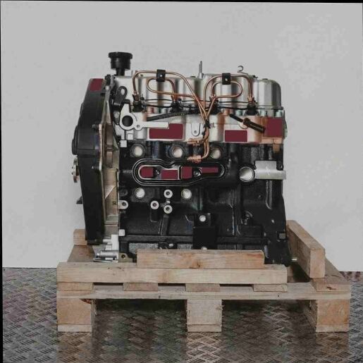 Motor 4D56 (8V) auf Holzpalette vor weißem Hintergrund. Der Motor, direkt von vorne fotografiert, zeigt silberne und schwarze Komponenten. Deutlich sichtbar sind Schläuche und Öffnungen.