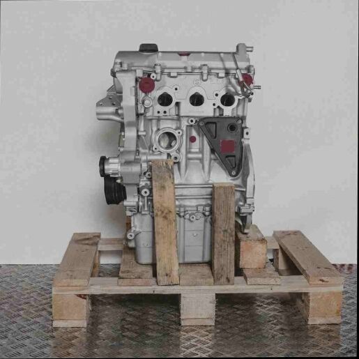 Seitenansicht des Motors M 132.910 auf einer Holzpalette vor weißem Hintergrund. Der Motor ist vertikal ausgerichtet und zeigt Schläuche und gelbe Verschlüsse.
