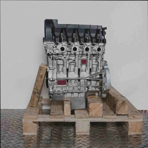 Seitenansicht eines Motors M 166.991 auf einer Holzpalette vor weißem Hintergrund. Der Motor, mit schwarzen und silbernen Komponenten, ist vertikal ausgerichtet.