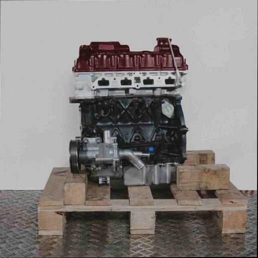 Seitenansicht eines schwarzen und silbernen Motors W10 B16 A auf einer Holzpalette vor weißem Hintergrund. Verschiedene Anbauteile wie Riemenscheibe und Rohr sind im Detail zu sehen.