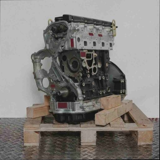 YD22ETI Motor auf Holzpalette vor weißem Hintergrund. Der Motor in Grautönen zeigt Details wie Ketten und Zahnräder. Aufnahme von der Seite.